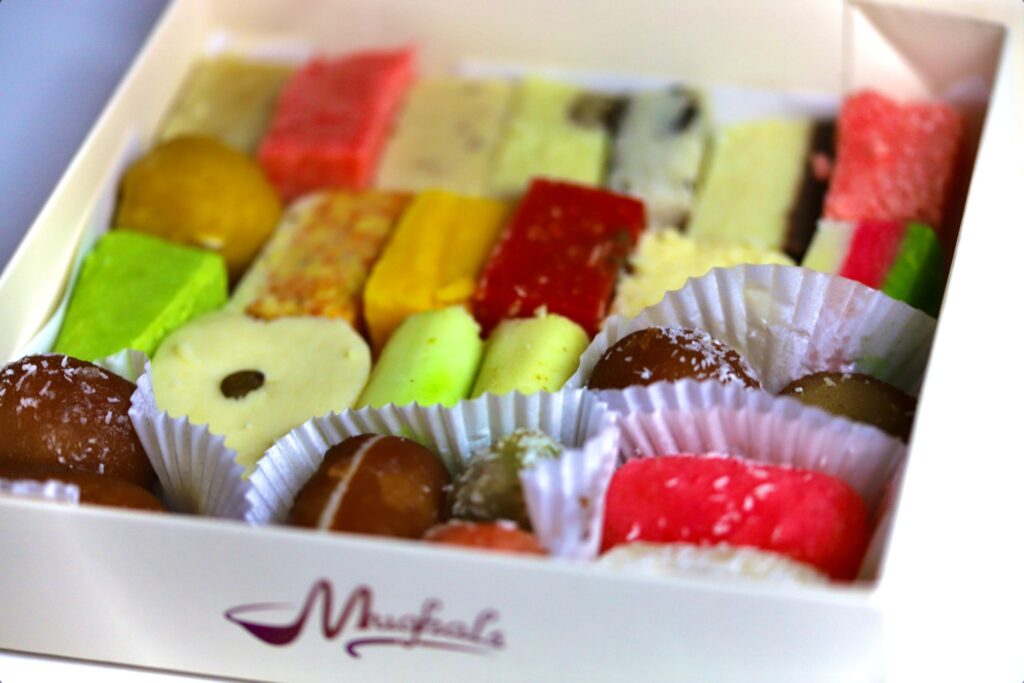 Traditional Pakistani and Indian sweets including Mithai, Gulab Jamun, and Barfi neatly arranged on a tray from Mughals Restaurant and Sweet Centre in Bradford